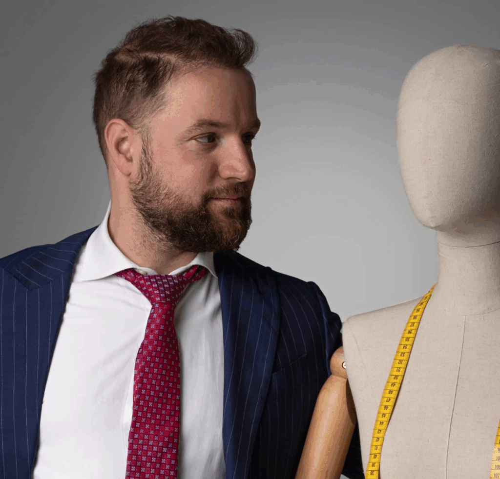Un uomo in abito gessato e cravatta rossa è in piedi accanto a una forma di vestito con un nastro di misurazione giallo drappeggiato sulle spalle.