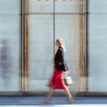 Una donna in abito rosso e blazer nero, che incarna l'eleganza, passa davanti all'ingresso di un negozio Gucci: una scena ispiratrice per chi è interessato a Produzione Abbigliamento Conto Terzi Piccole Quantità.