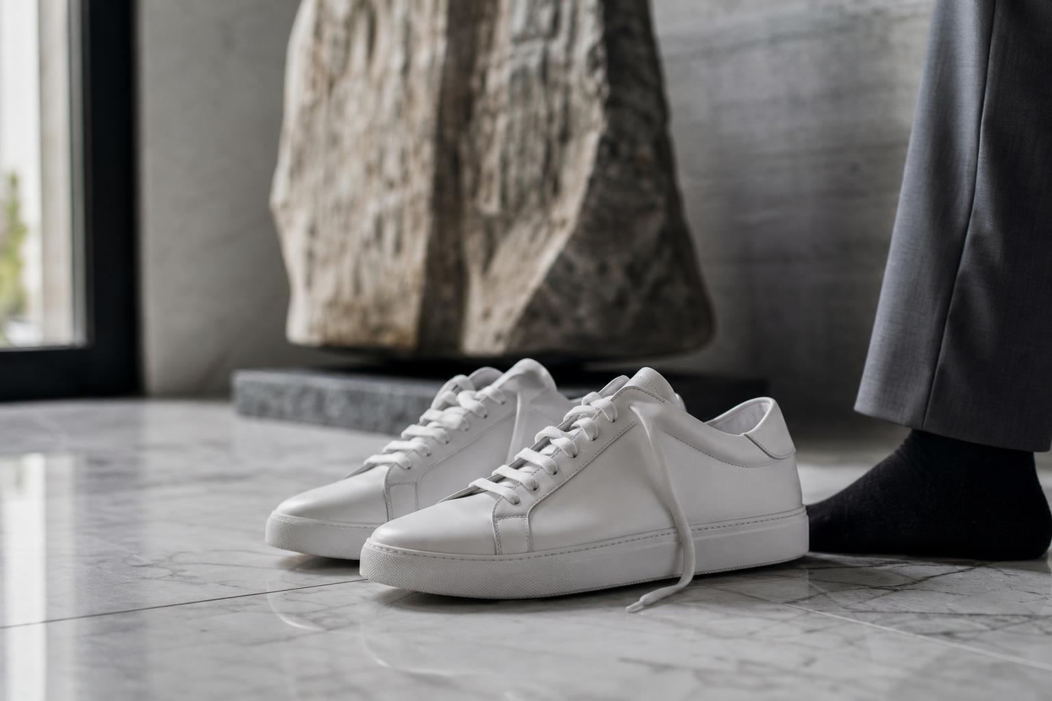 Studied Carelessness: paio di sneakers luxury minimaliste in pelle bianca su pavimento di marmo